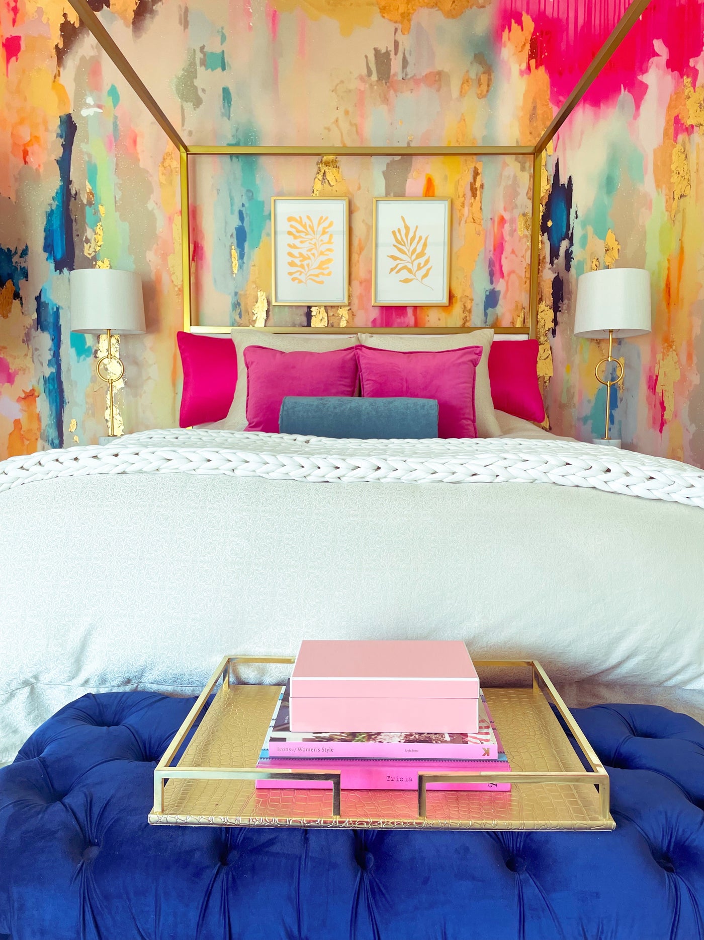 Decorative bedroom with bold colorful wall, bed with pink/blue pillows, and a tray with books.