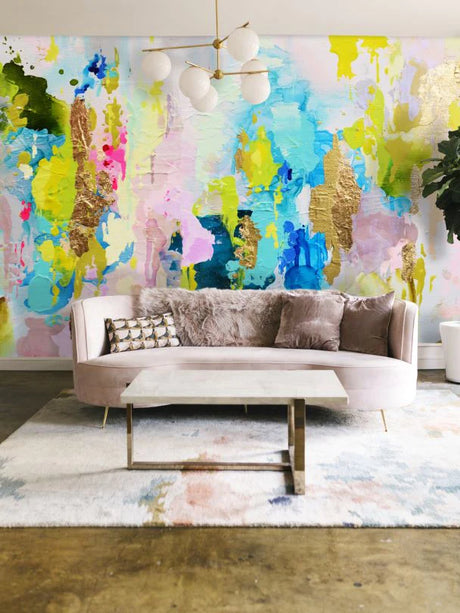 This living room decor pops with a burst of color from the chartreuse, lime and aqua abstract wallpaper design from women owned design shop, Vivian Ferne. The soft curved back sofa, pastel area rug and stone table delicately pull colors from the wallpaper to create a stunning combination between the wall art and the furniture. This wallpaper design includes real gold leafing for added texture and complexity.
