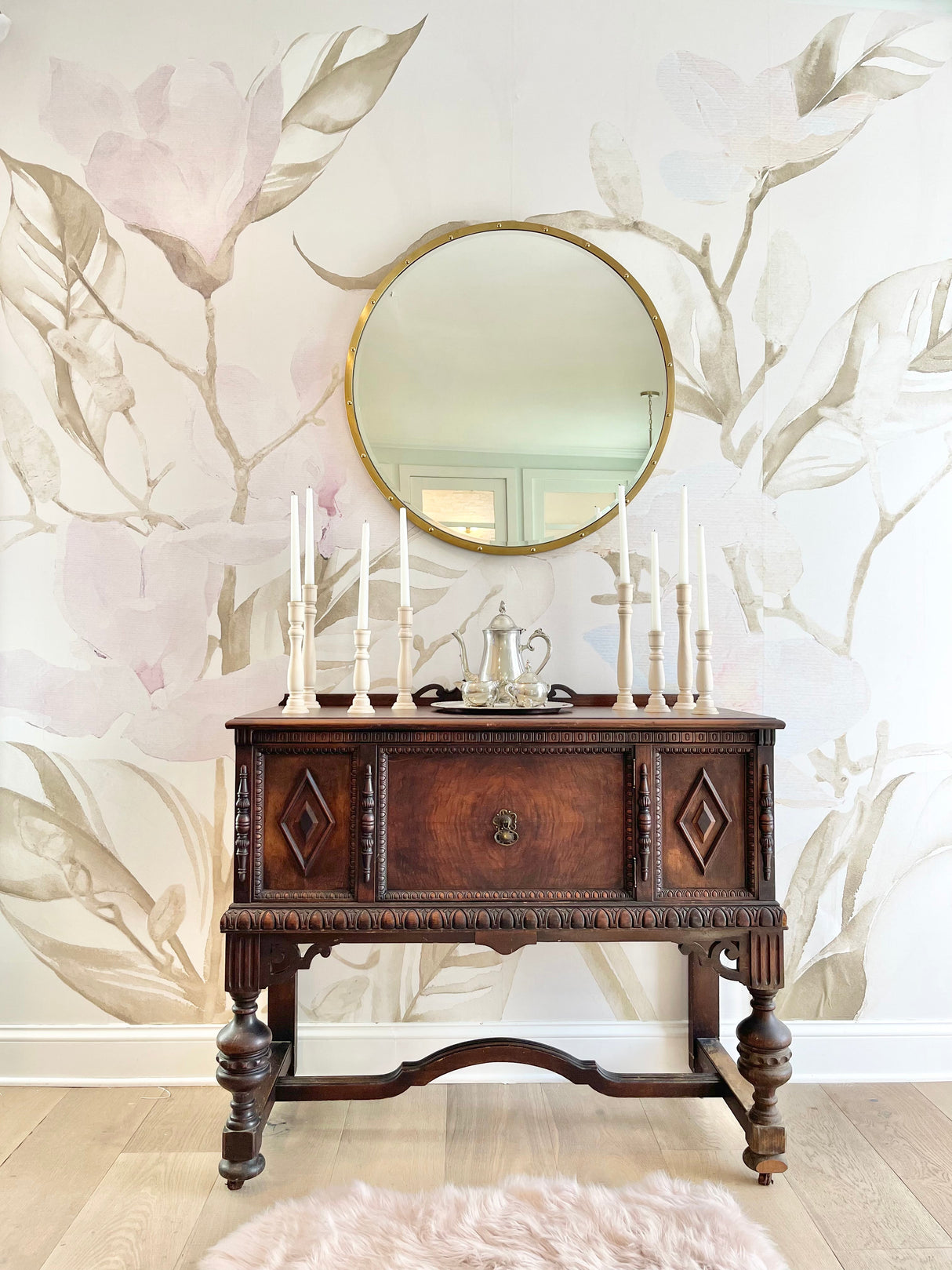 This luxury dining room accent wall features antique buffet table and wooden candle sticks. The wallpaper decor is a stunning large patter wallpaper with wispy magnolia leaves and dusted pink magnolia flowers. This wallpaper design is a perfect product for dining rooms, living rooms, bedrooms or reading areas in any home.