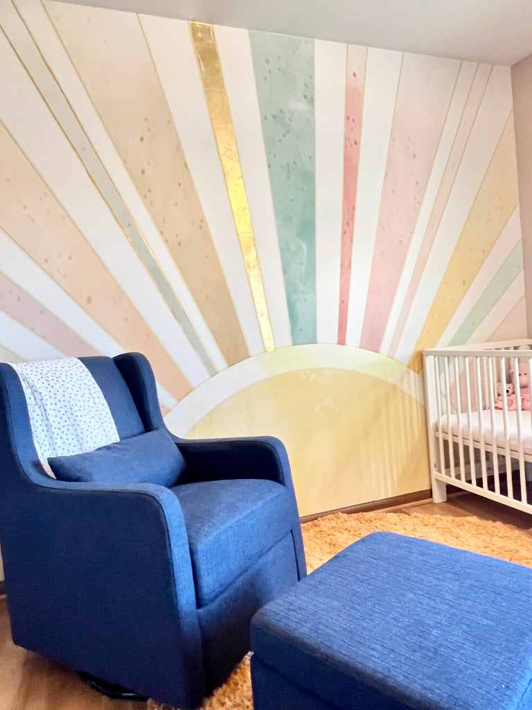 Blue rocking and and white crib sit in front of rainbow themed wallpaper in this colorful bright nursery interior design theme.