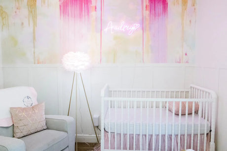 Pink themed nursery design with classic white wooden crib, gray love seat and a beautiful pink abstract wallpaper mural by designer, Vivian Ferne.