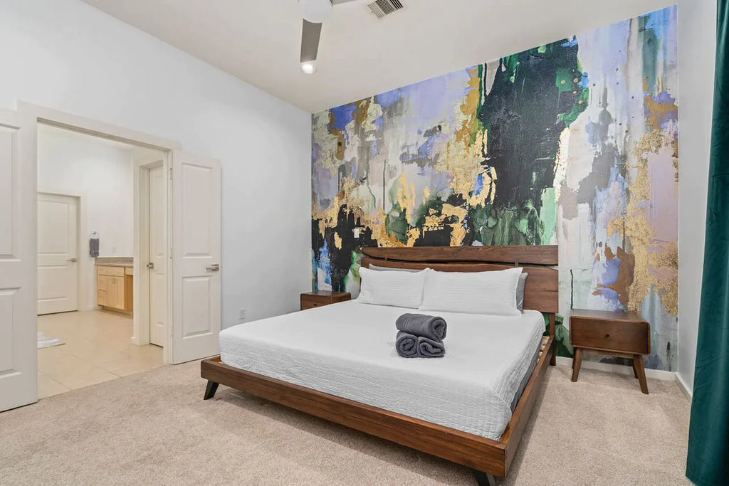 Airbnb decor featuring the green, chartreuse and gold wallpaper design. This design is a large scale abstract wallpaper installation. Other design elements in this photo include a modern wooden bed with white bedding, pillows and wooden side tables