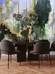 This staged dining room features modern decor and the abstract wallpaper design with green (kelly and emerald) gold, blue and grey. The design is inspired by the famous abstract artist Fran Maass who created the original image with acrylic paint and alcohol inks. The dining room features brown chairs, glass and wood tables, stemmed wine glasses and glass overhead lighting. The herringbone flooring creates a perfect foreground for this design concept.