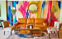 This wallpaper is shows in a maximalist living room with a leather sofa, glass book/coffee table, floral chairs and mirrors. This design is multi colored and is highly recommended for people looking at bold, high energy abstract wallpaper designs for their homes, boutique hotels, offices, vacation homes or airbnbs. Make your space unique with this stunning wallpaper design available in prepasted or peel and stick material as well as french lux.