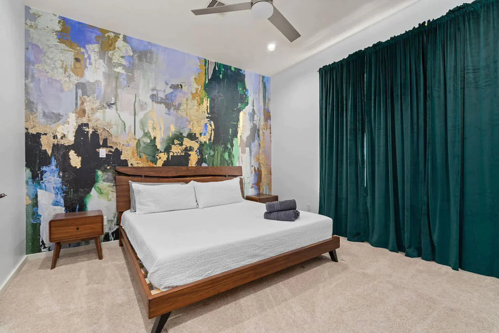 This customer installation was completed in an Airbnb. The interior design was centered around the large scale abstract design by Vivian Ferne. The greens, blues and chartreuse and gold are a stunning addition to this bedroom decor. The wooden bed frame and end tables are subtle decor decisions that allow the wallpaper mural to stand out in this bedroom. The application of this wallpaper product was with our Peel and Stick product. The mural is available in prepasted and French lux materials.  