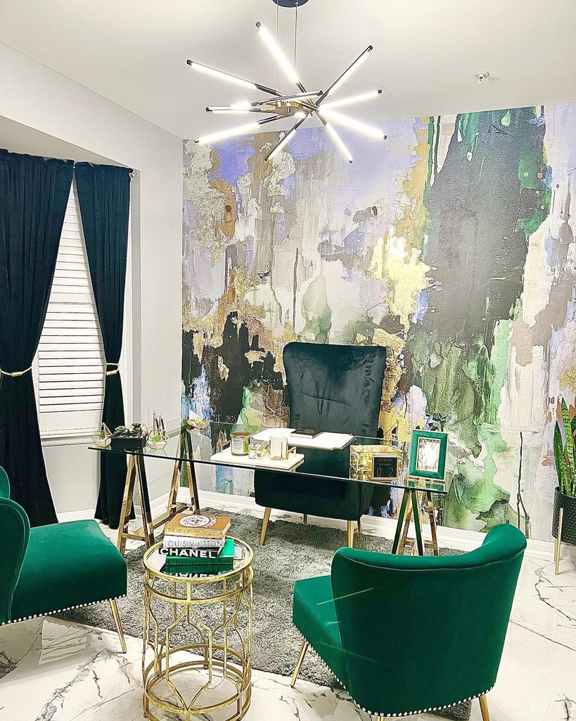 Luxury office space with modern suede furniture, glass and gold desk, modern light fixtures and marble floors. The backdrop for this office is the green, gold, chartreuse and blue abstract wallpaper design/.