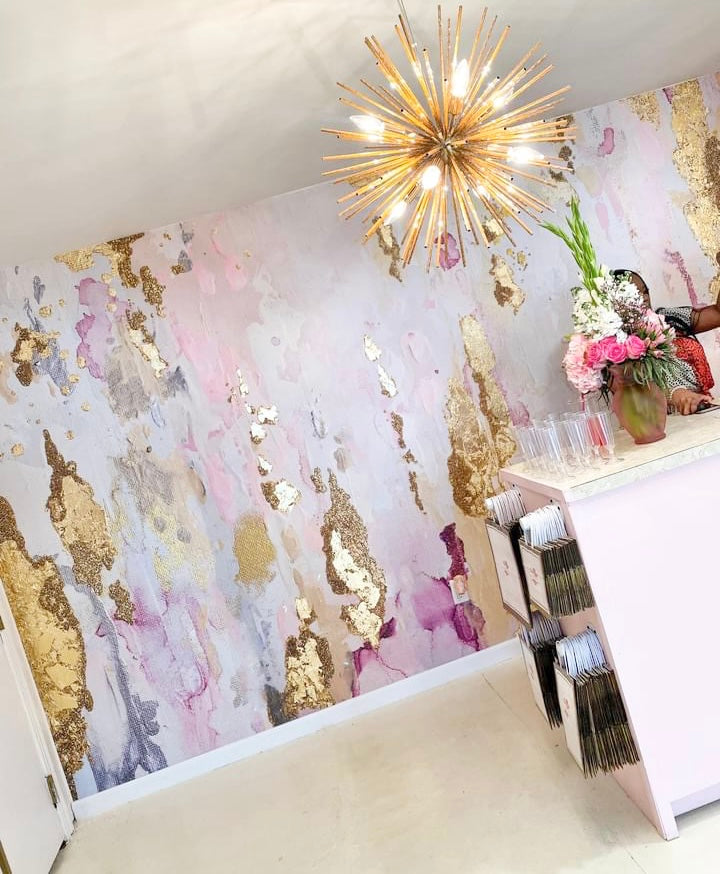 Decorative wall with gold and pink abstract design, gold starburst chandelier, and floral arrangement.