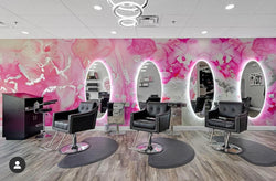 A front angle of a hair salon that features this pink and silver marble style wall decor. This wallpaper was designed using the original abstract painting created by Fran Maass. The wallpaper was applied using peel and stick materials and covers the feature wall of this hair salon. These wallpaper designs come in a variety of standard sizes as well as custom sizings. 