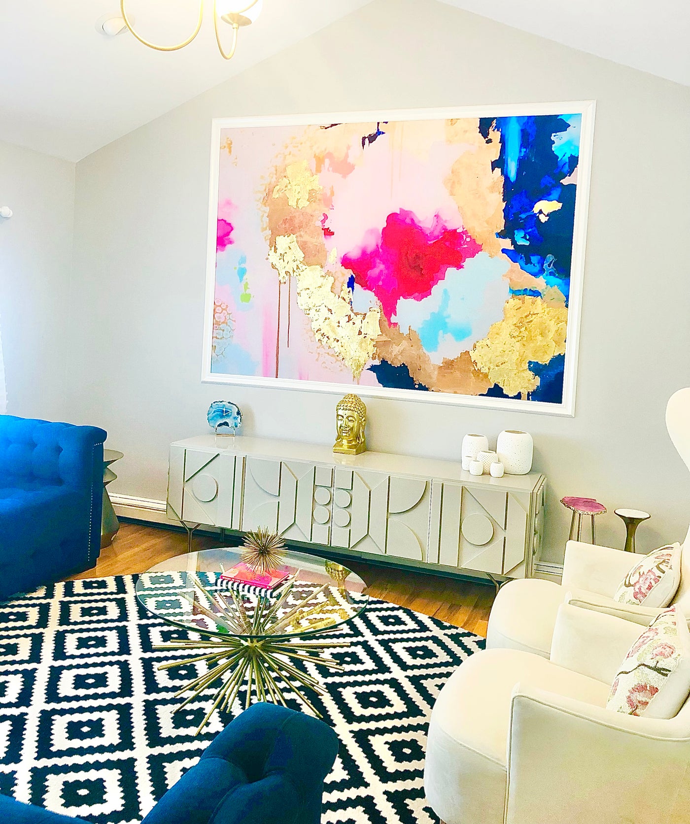 Living room with colorful abstract pink/blue "Sapphire" art, blue sofa, and white armchair.