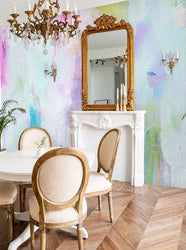 This classic dinning room interior space is freshly adorned with a modern pastel style wallpaper mural from famous interior designer, Vivian Ferne. This wallpaper is created from an original abstract painting and features soft blues, pinks, greens and turquoise colors. This designs adds a burst of color to living rooms, bedrooms, hotels, spas and salons. The interior space also features herringbone floors, gold framed mirrors and victorian era decor.