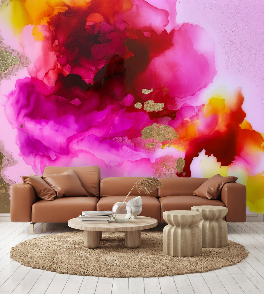 Luxury brightly themed living room decor featuring a large scale abstract pink, fuchsia and yellow wallpaper. The room showcases a mid-century leather sofa and stone decorative tables. Light wood flooring is covered with an ornate rug. This look is perfect for any modern, luxury living room space, spas, hotels or airbnbs.