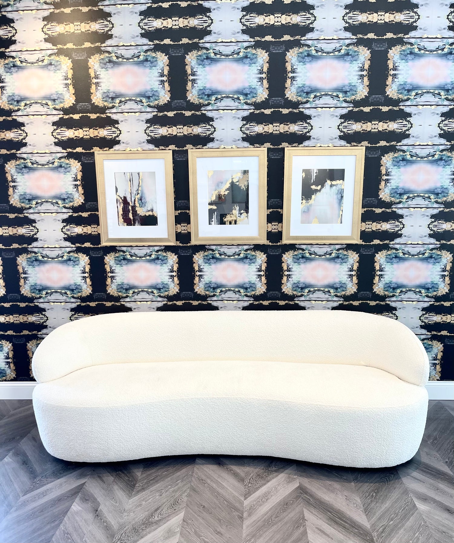 Living room wall decor with framed gold prints, curved back sofa and large pattern repeating wallpaper.