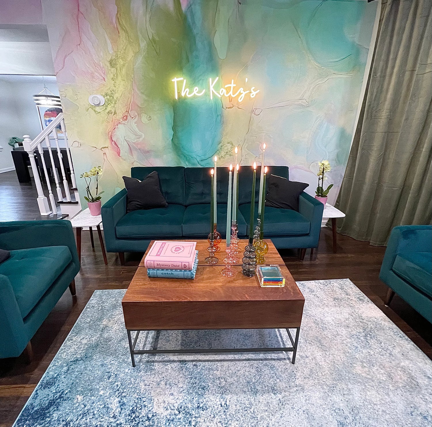 Luxury living room interior design staged with green suede couch set, wood coffee table, decorative candles and abstract wallpaper design. Blue area rug with white marble end tables.