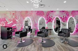 A front angle of a hair salon that features this pink and silver marble style wall decor. This wallpaper was designed using the original abstract painting created by Fran Maass. The wallpaper was applied using peel and stick materials and covers the feature wall of this hair salon. These wallpaper designs come in a variety of standard sizes as well as custom sizings.