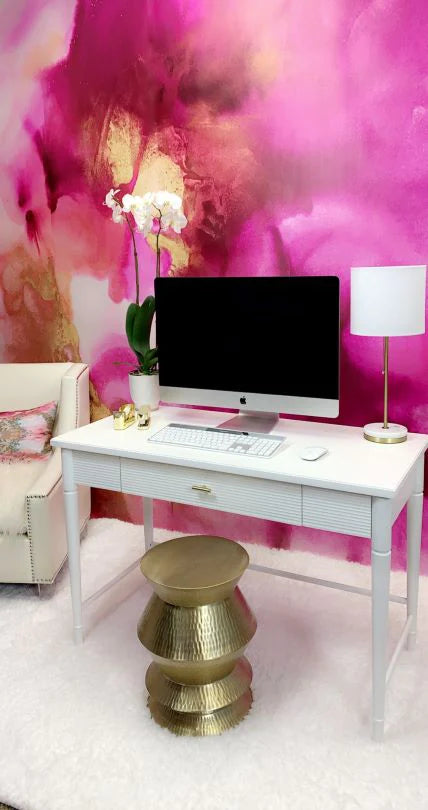 This office space was decorated with the stunning pink, tangerine and gold wallpaper from Vivian Ferne. This product is available in prepasted, peel and stick and french lux materials. The office space decor includes a white desk, apple imac, gold stool, and white love chair. Additional features are white lamp, white rug and orchids.