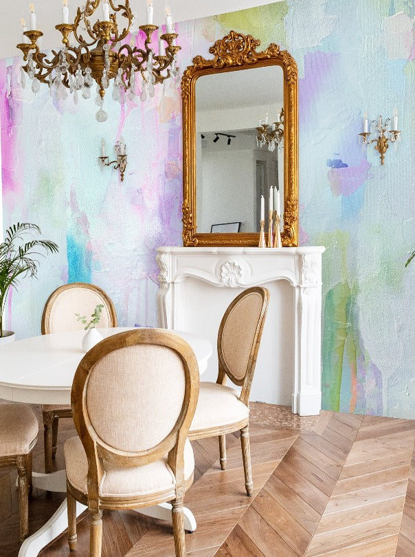 This classic dinning room interior space is freshly adorned with a modern pastel style wallpaper mural from famous interior designer, Vivian Ferne. This wallpaper is created from an original abstract painting and features soft blues, pinks, greens and turquoise colors. This designs adds a burst of color to living rooms, bedrooms, hotels, spas and salons. The interior space also features herringbone floors, gold framed mirrors and victorian era decor.