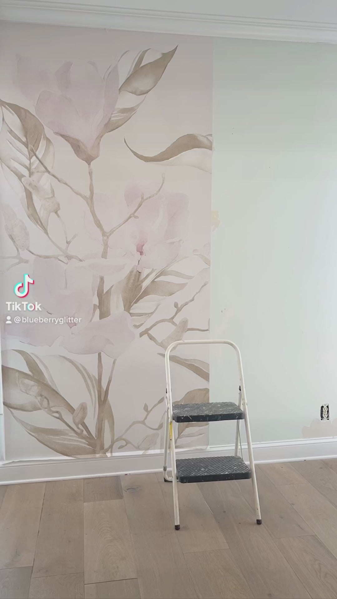 Installing the magnolia themed large pattern wallpaper for this dining room accent wall. This shoot features an antique buffet table, candles, mirrors white baseboard and magnolia themed wallpaper.