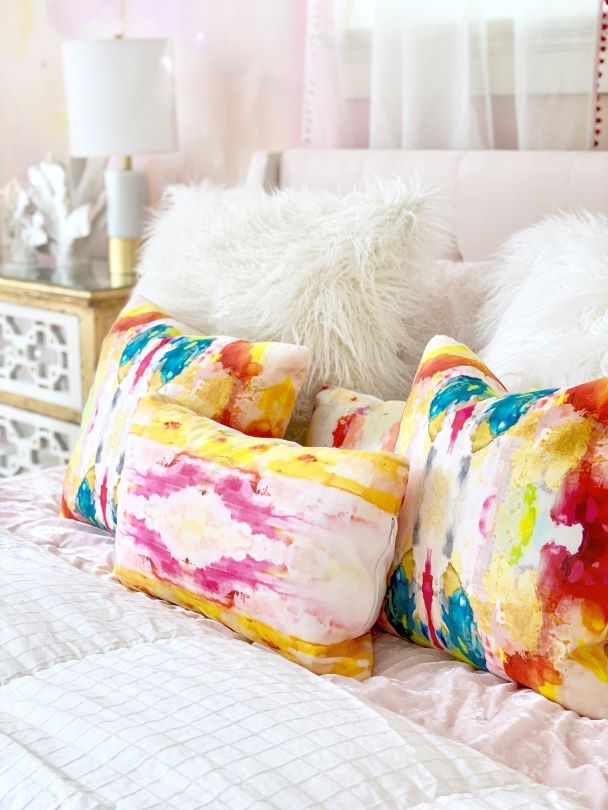colorful throw pillow on white bedding with gold accents